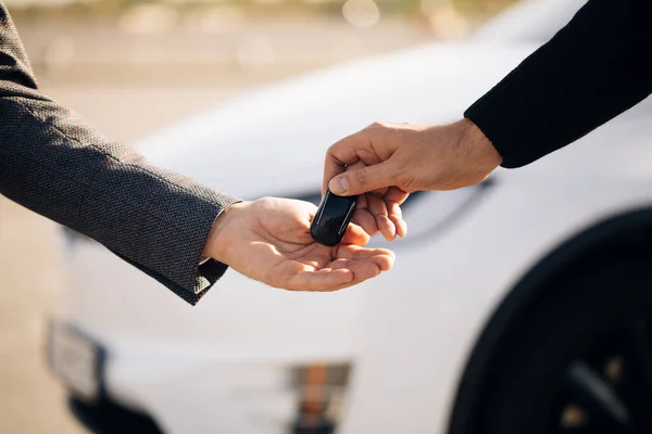 Mão masculina dá uma chave de carro para a mão masculina na concessionária de carro de perto. Vendedor de automóveis não reconhecido e um homem que comprou um veículo. Negociante dando a chave para o novo proprietário em auto show ou salão — Fotografia de Stock