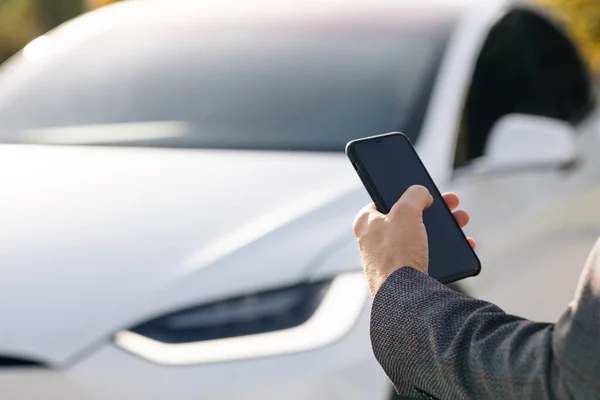 Osoba ovládá samojízdné elektrické auto pomocí mobilní aplikace. Autonomní autopilot auto bez řidiče. Aplikace Smartphone. Senzory pátrají po vozidlech, nebezpečí, omezení rychlosti. — Stock fotografie