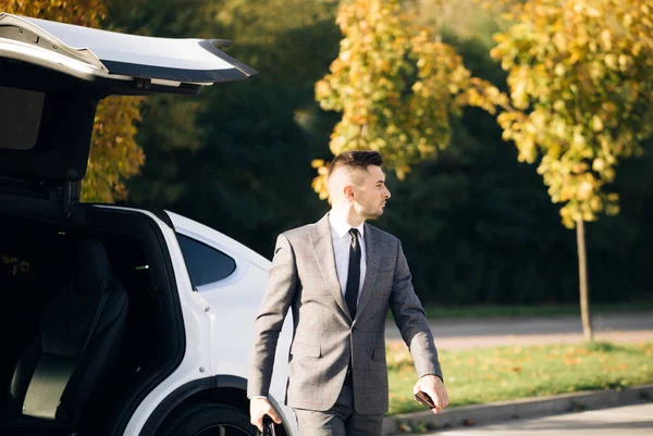 Stylish man getting out of car, personal chauffeur bringing businessman. Business man with briefcase get out from auto and walking to office building
