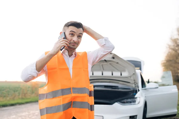 Mannen som pratar i telefon och tittar på bilmotorn. ung man använda smartphone, stading på vägen nära den trasiga bilen öppnade motorhuven, ringa bilassistans, hjälpa till att reparera. — Stockfoto