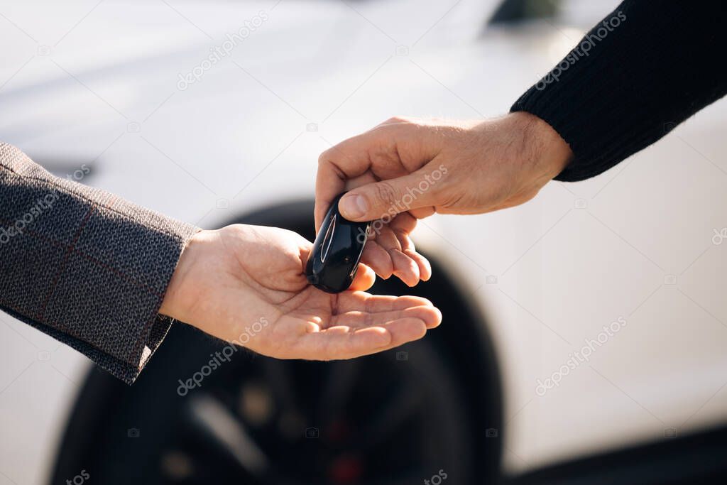 Dealer giving key to new owner in auto show or salon. Male hand gives a car keys to male hand in the car dealership close up. Unrecognized auto seller and a man who bought a vehicle.