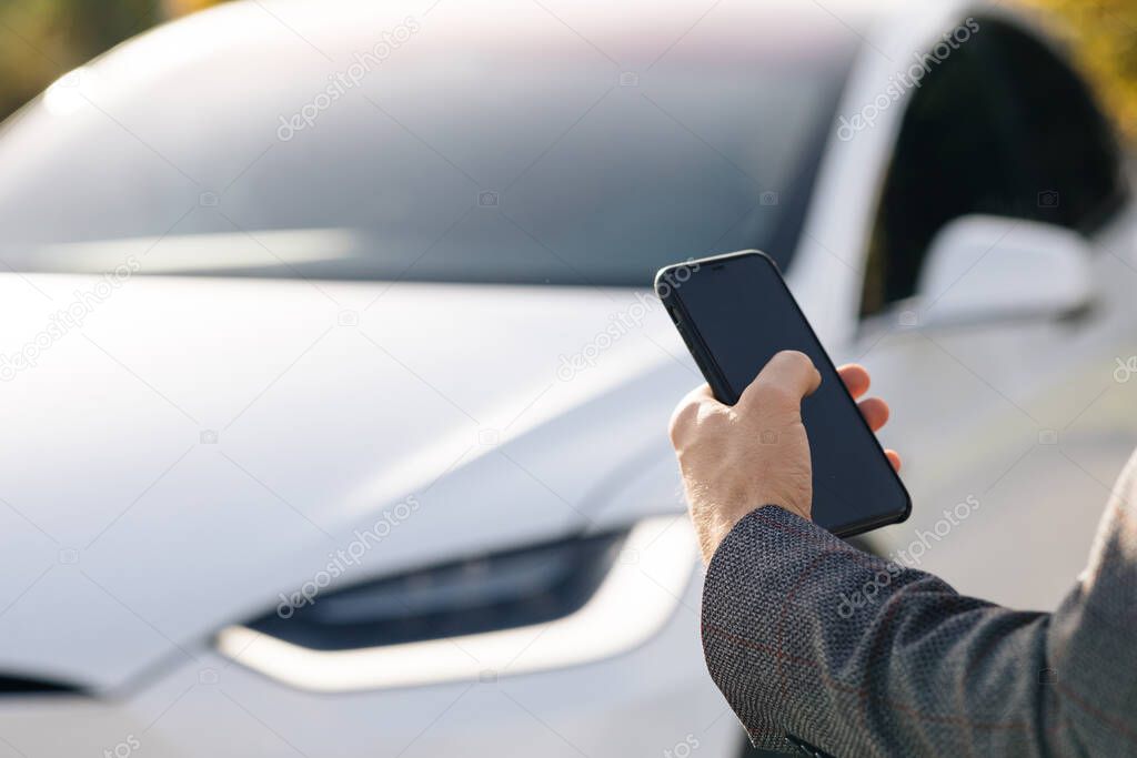 Person controls a self-driving electric car using mobile application. Autonomous autopilot driverless car. Smartphone app. Sensor scanning road ahead for vehicles, danger, speed limits.