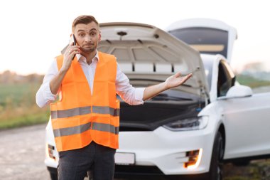 Elektirikli arabası bozulduğu için araba tamircisini arayan adam. Konsept yol kazası. Tamir etmeye. Çelik yelekli bir adam cep telefonuyla konuşuyor.