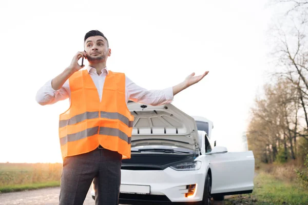 Vit man har brutit ner elbilen på vägen han pratar i telefon för att ringa någon för att hjälpa eller mekanik bilservice. Bilolycka. Bilproblem — Stockfoto