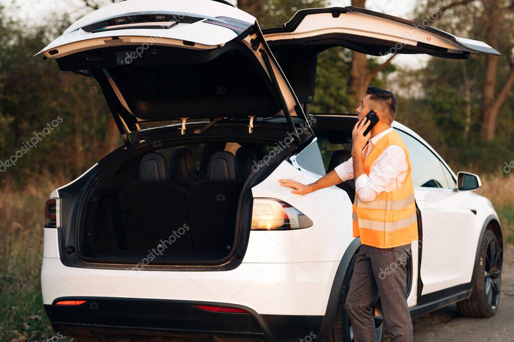 Unhappy businessman speak on phone near the broken electric car help repair stress problem emergency insurance auto. Man calling car assistance services. Concept road accident. Help repair.