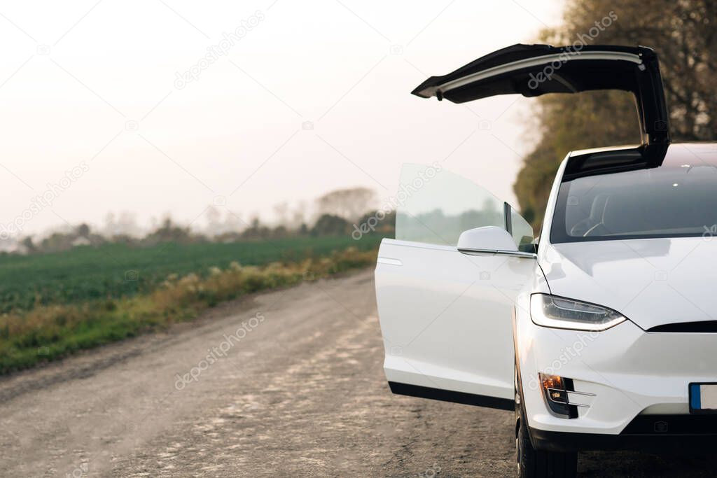 Luxury modern vehicle along trees and fields. Electric Car on Country Road. Electric Car on Gravel road with trees at sunset.