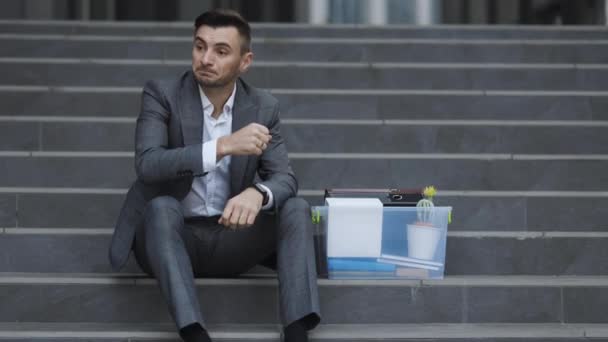 Verzweifelte männliche Büroangestellte verloren ihren Job. Arbeitslosenquote steigt wegen Pandemie. Geschäftsmann sitzt auf Treppe in der Nähe von Bürozentrum mit Box und Dokumenten als verlorenen Job — Stockvideo