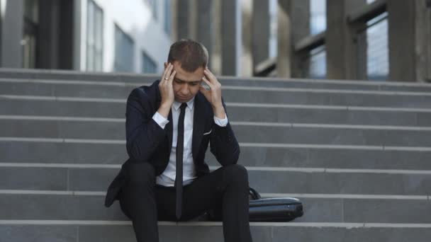Pracownik biurowy w rozpaczy stracił pracę. Zwolniony nieszczęśliwy brodaty Europejczyk traci pracę siedząc na schodach. Zdenerwowany młody biznesmen w frustracji poza biurem. Bezrobocie. Kryzys — Wideo stockowe