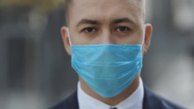 Tıbbi maskeli genç ve yakışıklı iş adamının yüzü mutlu bir şekilde kameraya bakıyor. Sokaktaki adamın portresi. Coronavirus konsepti