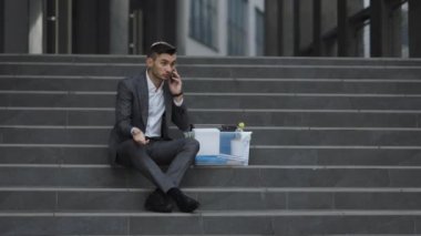 Takım elbiseli, dışarıda merdivenlerde oturan işsiz genç bir erkek. Kovulan adam telefonda kutudaki eşyalarla konuşuyor. Cep telefonu sohbeti. Telefonda konuşuyorum.