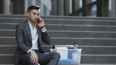 Kovulan adam telefonda kutudaki eşyalarla konuşuyor. Cep telefonu sohbeti. Telefonda konuşuyorum. Dışarıdaki merdivenlerde oturan resmi takım elbiseli, yakışıklı, işsiz bir ofis çalışanı.