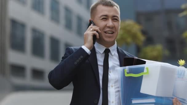 Glad avskedad man som pratar i telefon med saker i lådan. Mobilsamtal. Jag talar i telefon. En anställd mellan kontorsbyggnader med låda och dokument med skrivbordsblomma — Stockvideo