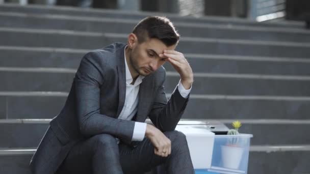 Retrato triste hombre de negocios sentado en las escaleras al aire libre con caja de cosas como negocio perdido. Hombre despedido. Un oficinista desesperado perdió su trabajo. Tasa de desempleo creciente debida a pandemia — Vídeos de Stock