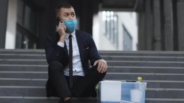 Resmi takım elbiseli ve koruyucu maskeli, merdivenlerde oturan yakışıklı, işsiz bir ofis çalışanı. Kovulan adam telefonda kutudaki eşyalarla konuşuyor. Cep telefonu sohbeti. Telefonda konuşuyorum.