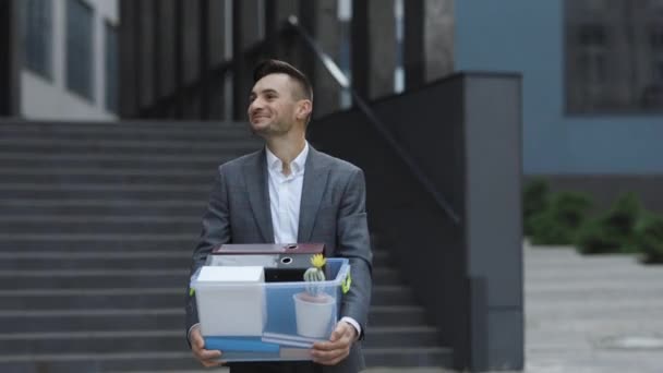 Ein männlicher Büroangestellter mit einer Kiste voller persönlicher Dinge tritt von seinem Job zurück. Business-Stil-Anzug. Coronavirus im Freien soziale Distanzierung. Finanzen und Industrie — Stockvideo