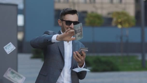 Money rain, falling dollars. Successful business concept. Successful Businessman in a Suit Wear Sunglasses Throwing Money in the Camera Standing in the Street near Office Building — Stock Video