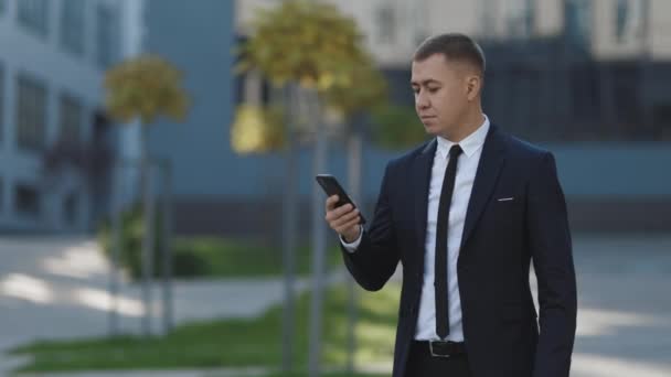 Homme d'affaires prospère célébrant gagner avec téléphone portable à l'extérieur. Surpris homme regardant téléphone portable dehors. Portrait d'homme excité lisant de bonnes nouvelles sur smartphone en plein air. — Video