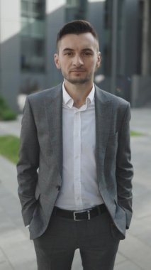 İş dışında duran takım elbiseli yakışıklı girişimcinin dikey videosu. Başarılı bir iş adamı. Kurumsal insanlar. Ofis müdürü. İş adamı iş merkezinin yakınındaki kameraya bakıyor.