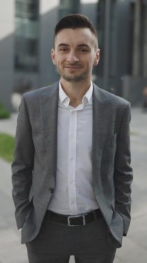 Takım elbiseli patronun kendine güveninin dikey videosu. Yakışıklı iş adamının portresi iş merkezinin yakınındaki kameraya bakıp gülümsüyor. Kurumsal insanlar. Ofis yöneticisi.