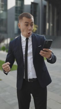 Mutlu iş adamı iyi haber mesajı alıyor. Heyecanlı erkek kazanan akıllı telefona bakarak başarıyı kutluyor. Mobil zafer konsepti. Dikey Ekran Yönelimi 9: 16.