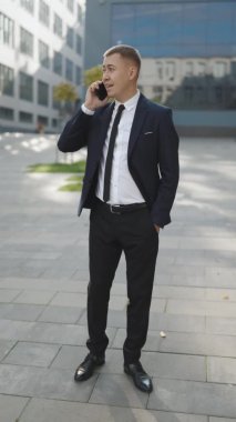 Dışarıda telefonla konuşan yakışıklı bir adam portresi. Sokakta akıllı telefondan konuşan bir iş adamı. Dışarıdaki adamı ara. Dikey Ekran Yönelimli Video Görüntüsü 9: 16.
