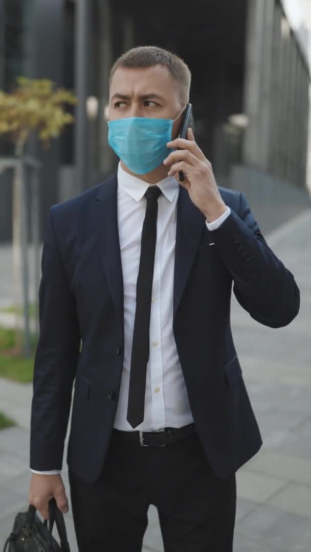 Hombre de negocios joven caucásico con máscara médica hablando por teléfono. COVID-19 Infección por Coronavirus. Máscara facial Covid-19. Epidemic Coronavirus Mers. Human Masked 2019-ncov. Video con pantalla vertical. — Vídeos de Stock