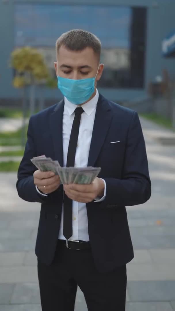 Business Man in Protective Face Mask räknar Cash. Karantänfinanskris. Ung stilig rik man bär stilig kostym räkna pengar stående på gatan nära Office Building Vertikal Video — Stockvideo