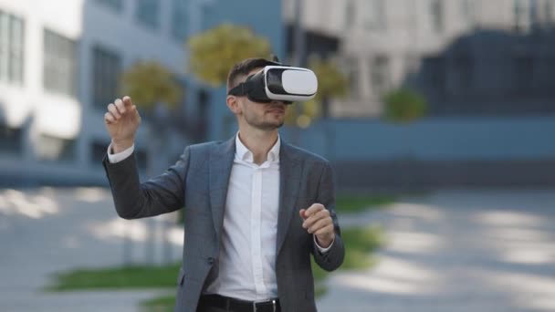 Un bărbat frumos care poartă căști de realitate virtuală. Realitatea augmentată. Omul de afaceri atinge ceva folosind ochelari 3D moderni în apropierea clădirii de birouri. Această nouă tehnologie oferă noi dimensiuni 3D — Videoclip de stoc
