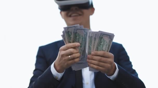 Bohatý muž ve VR sluchátkách počítá peníze a usmívá se. Mladý obchodník stojí s balíčkem dolarů. Bohatství a úspěch konceptu. Nová technologie nabízí nové 3D rozměry. — Stock video