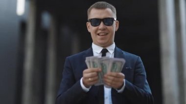 Başarılı bir iş adamı para sayıyor. Gülümseyen adam modern ofisin yanında iyi anlaşmalardan hoşlanır. Adam kolay para kazanıyordu. Şık takım elbiseli, güneş gözlüklü, para sayan zengin bir adam..