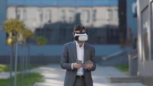 Concepto de riqueza y éxito. La nueva tecnología ofrece nuevas dimensiones 3D. Hombre rico con auriculares VR contando dinero. Joven empresario de pie con paquete de dólares — Vídeo de stock