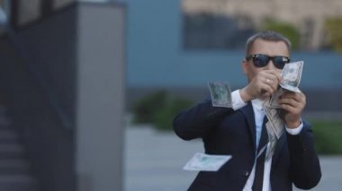 Komik adam para saçıyor. Genç mutlu işadamı paraları ofis merkezinin yakınındaki sokağa saçıyor. Para yağmuru, düşen dolarlar. Başarılı bir iş.
