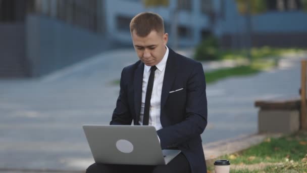 Homem de negócios caucasiano de terno e gravata comunicação enquanto digita no laptop sentado fora. Trabalho à distância. Homem isolado em um terno — Vídeo de Stock