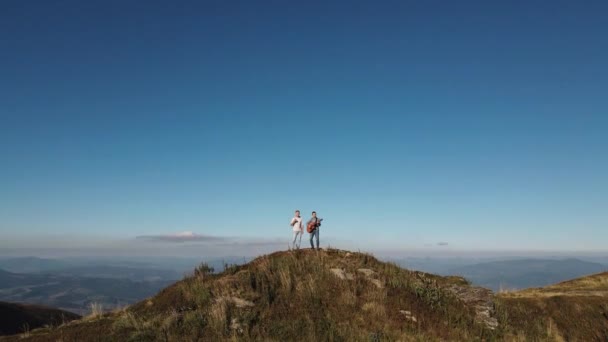 Músico tocando instrumentos durante o pôr do sol sobre a luz do sol. Vista aérea de dois jovens músicos tocando instrumentos acústicos nas montanhas. Homens tocando violão na natureza — Vídeo de Stock