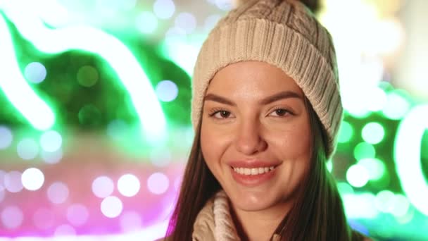 Porträt einer fröhlichen kaukasischen Frau mit Hut, die in die Kamera lächelt, um die Weihnachtsbeleuchtung in der Innenstadt anzuschauen. Positive Stimmung glückliche Emotion im Freien — Stockvideo