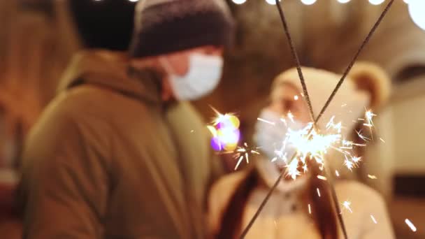 Unrecognizable Couple Hands holding and waving sparklers. Party on occasion of New Year, Christmas Eve or Xmas. Lifestyle. Couple in protective medical masks standing on the street holding sparklers — Stock Video