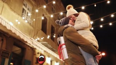 Çekici genç bir kadın, Noel partisinde erkek arkadaşıyla buluşuyor. Birbirlerine sıkıca sarılıyorlar ve sokakta sallanıyorlar. Güzel bir aşk çifti. Aydınlanma. Dışarıdaki mutlu çift. 4k Ağır çekim.