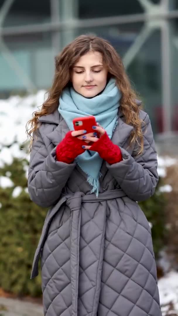 Retrato vertical de jovem bela mulher encaracolada em roupas de inverno segurando telefone celebrar boa oferta notícia móvel surpresa. Mulher excitada vencedora gritando sim alegrando sucesso olhando para o celular — Vídeo de Stock