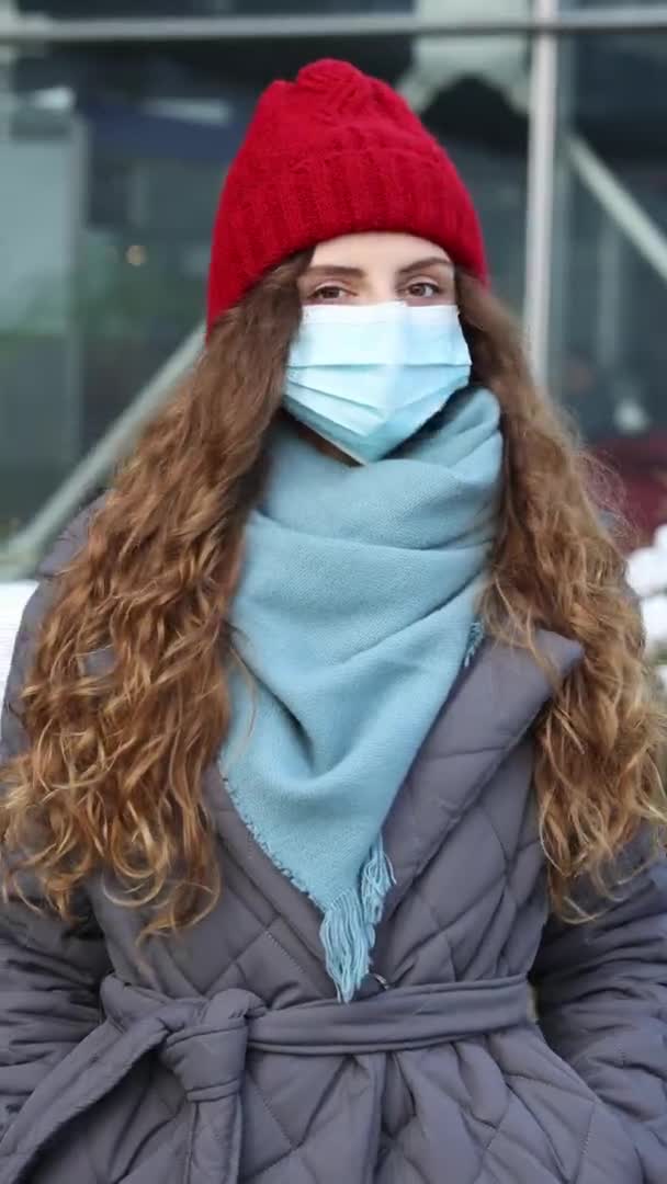 Vertikální snímek portrétu mladé kudrnaté ženy v masce lékařské tváře stojící na ulici. Pandemický virus chřipkové korony. Epidemie koronaviru. Dav lidí nemocný covid-19 — Stock video
