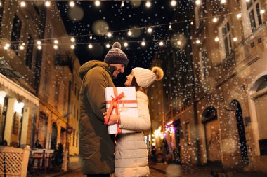 Noel hediyesi değişimi. Xmas birlikte kutluyor. Gülümseyen bir çift Noel arifesini parlak bir çelenkle kutluyor..