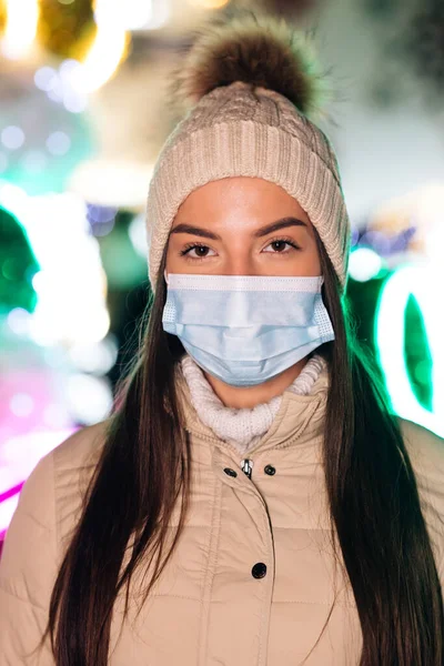Potret perempuan Kaukasia dalam topeng wajah medis berdiri di kota xmas yang didekorasi. Orang-orang sakit covid-19. Epidemic coronavirus. Virus flu korona pandemik. — Stok Foto