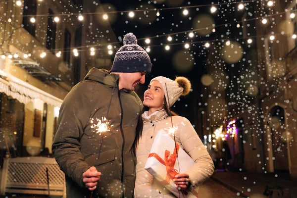 Geliefden reizen naar Europa op het hoogtepunt van de kerstvakantie. Liefjes in het centrum van de stad. Romantisch koppel in liefde met geschenk doos knuffelen en branden van de sterretjes. — Stockfoto