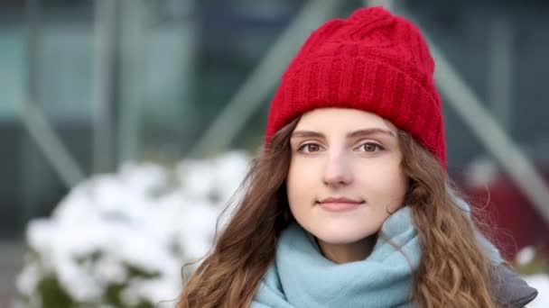 도시 중심가에 있는 빨간 모자를 쓰고 진지하게 곱슬곱슬 한 젊은 여성이 카메라를 쳐다 봅니다. 방석 소녀는 겨울 거리에 서 있다. 4k 느린 동작 — 비디오