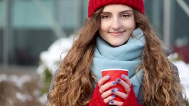 도시 배경에 커피 잔을 들고 있는 겨울 패션은 아름답고 화려 한 갈색이다. 행복, 겨울 휴일, 크리스마스, 음료, 사람들의 개념. 겨울 거리에 서 있는 귀에 거슬리는 암컷. — 비디오