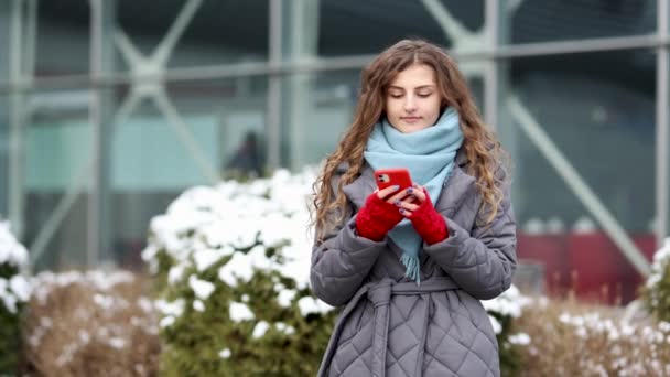 Porträtt av ung vacker lockig kvinna i vinterkläder innehav telefon fira goda mobila nyheter överraskning bud. Spännande kvinna vinnare skriker ja glädjande framgång tittar på mobiltelefon — Stockvideo