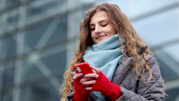 Kudrnaté ženské textovky na smartphonu stojící na ulici v Winter City. Ženské klepání na mobil venku. Dovolená venku. Šťastná mladá žena si užívá života. — Stock video