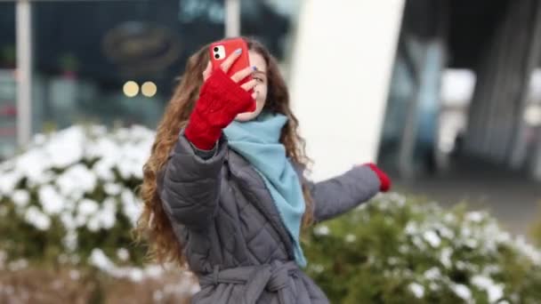 La bloguera está haciendo videos hablando para su página social en la calle en invierno. Vacaciones invierno chica rizada al aire libre. Estar en línea, redes sociales — Vídeos de Stock