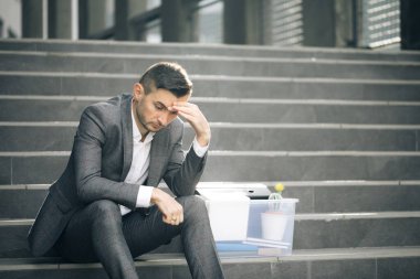 Çaresizlik içindeki erkek ofis çalışanı işini kaybetti. Mutsuz işadamı elinde bir kutu ıvır zıvırla merdivenlerde oturuyor. Kovulmuş adam. İşsizlik oranı pandemik olarak artıyor