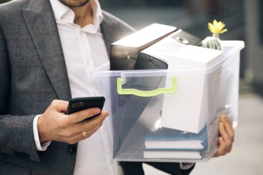 İş adamı iş merkezinin yanındaki telefonu kullanır. Bir kutu kişisel eşyası olan bir iş adamı telefon mesajlaşması kaydırağını kullanıyor. Portre elbisesi kariyer ofisi yakışıklı teknolojisi