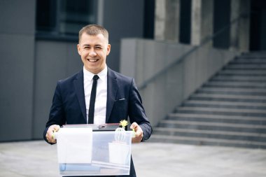 Bir kutu kişisel eşyası olan mutlu erkek ofis çalışanı portresi. İşsizlik kavramı. Parasız kaldı. İş adamı işini kaybetti. Kovulan adam dışarıda. Mutlu İşsiz kişi